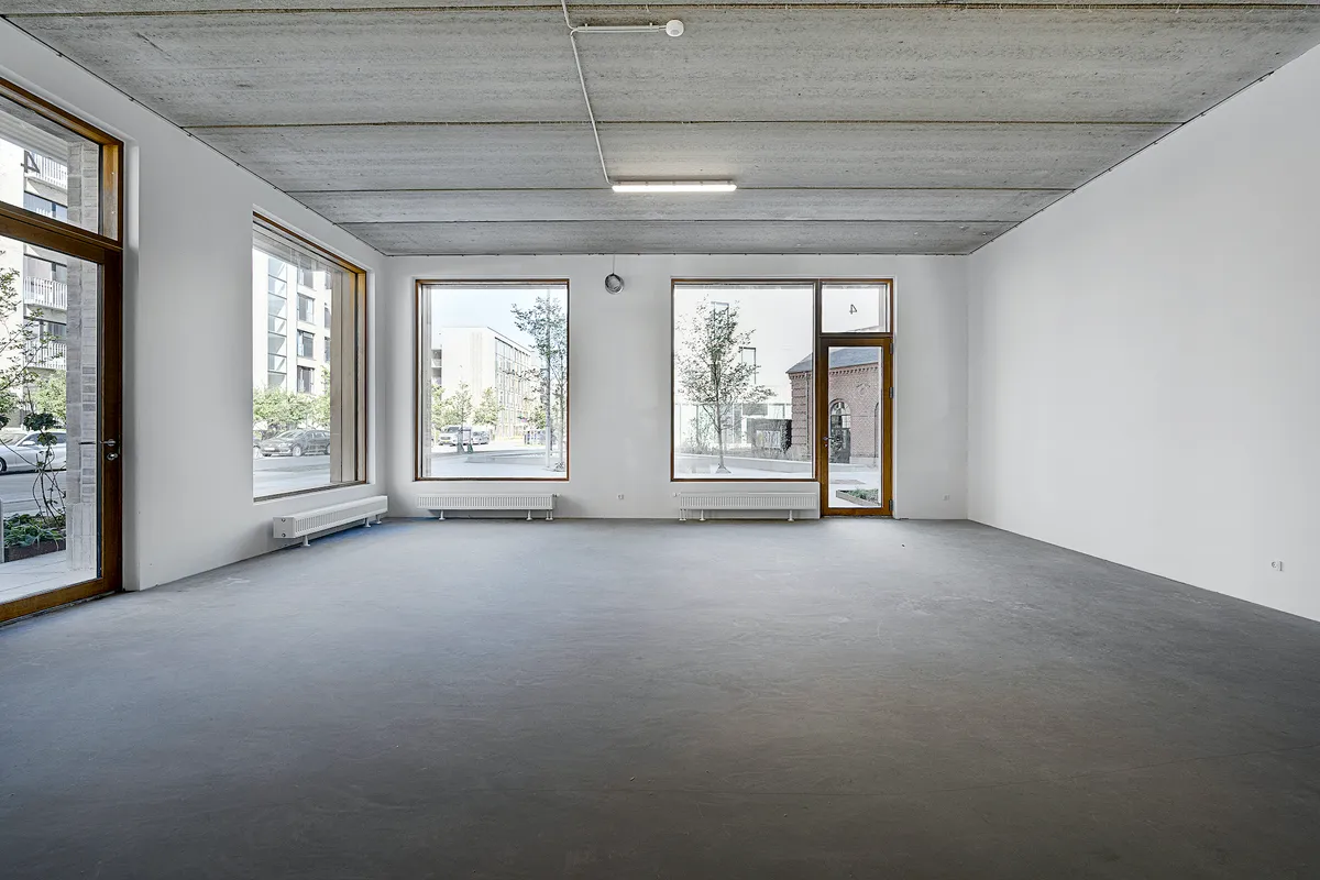 Et tomt rum med hvide vægge og gulv, tre store vinduer og lysekroner og radiatorer på væggene