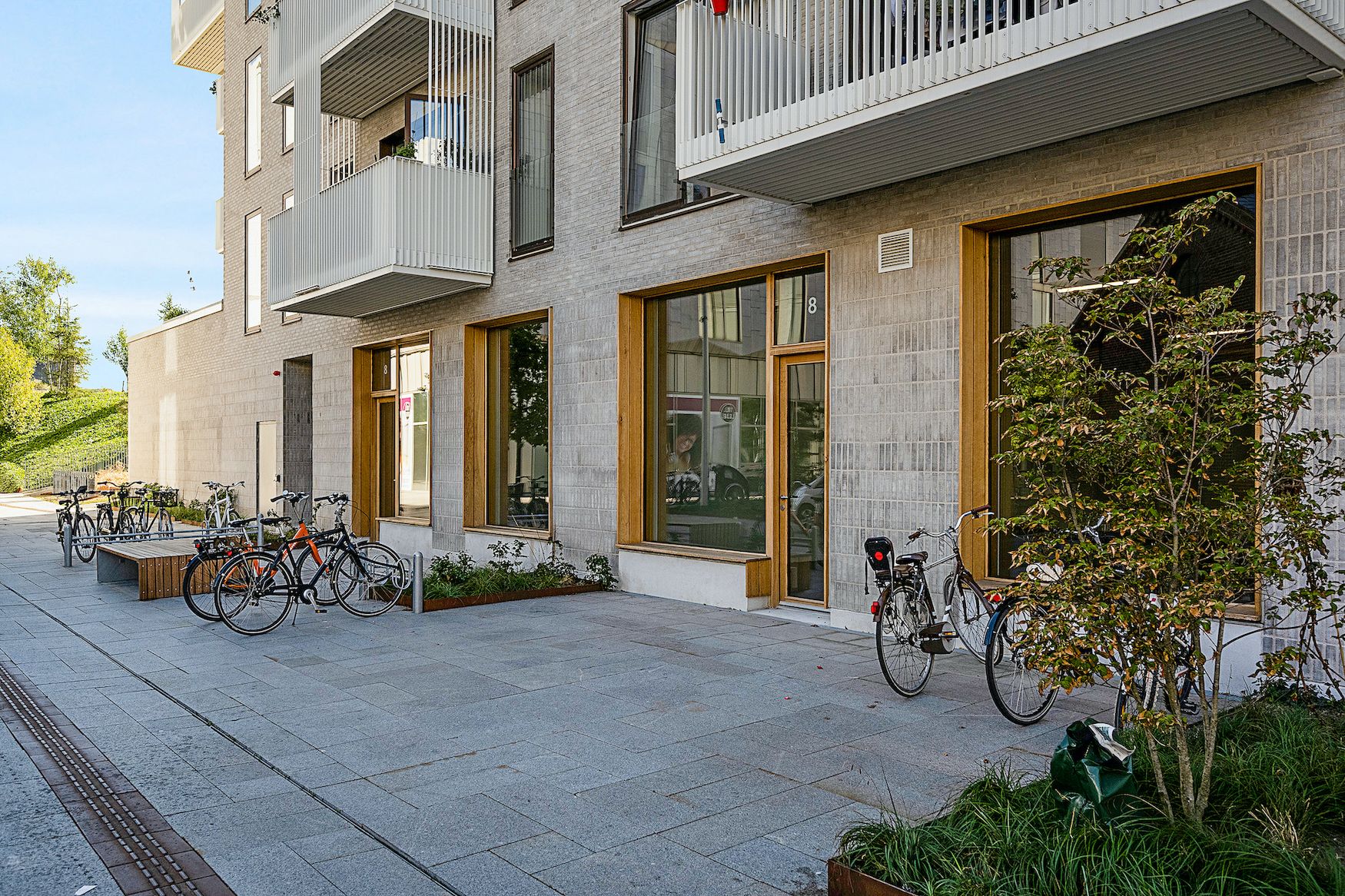 Bygning med fire vinduer og fire balkoner. Foran er en række cykler, en bænk og en plante i en pot.