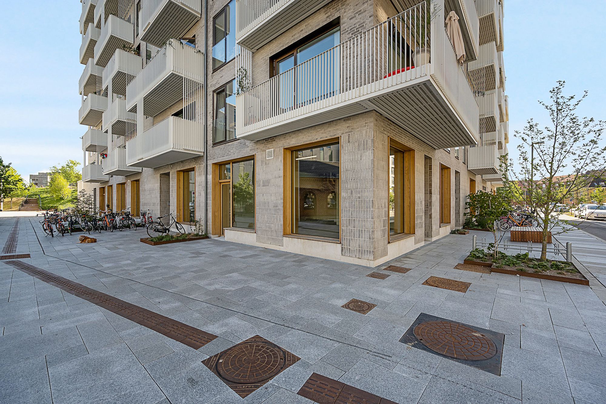 En stor hvid bygning med terrasser og parkerede cykler og planter i forgrunden