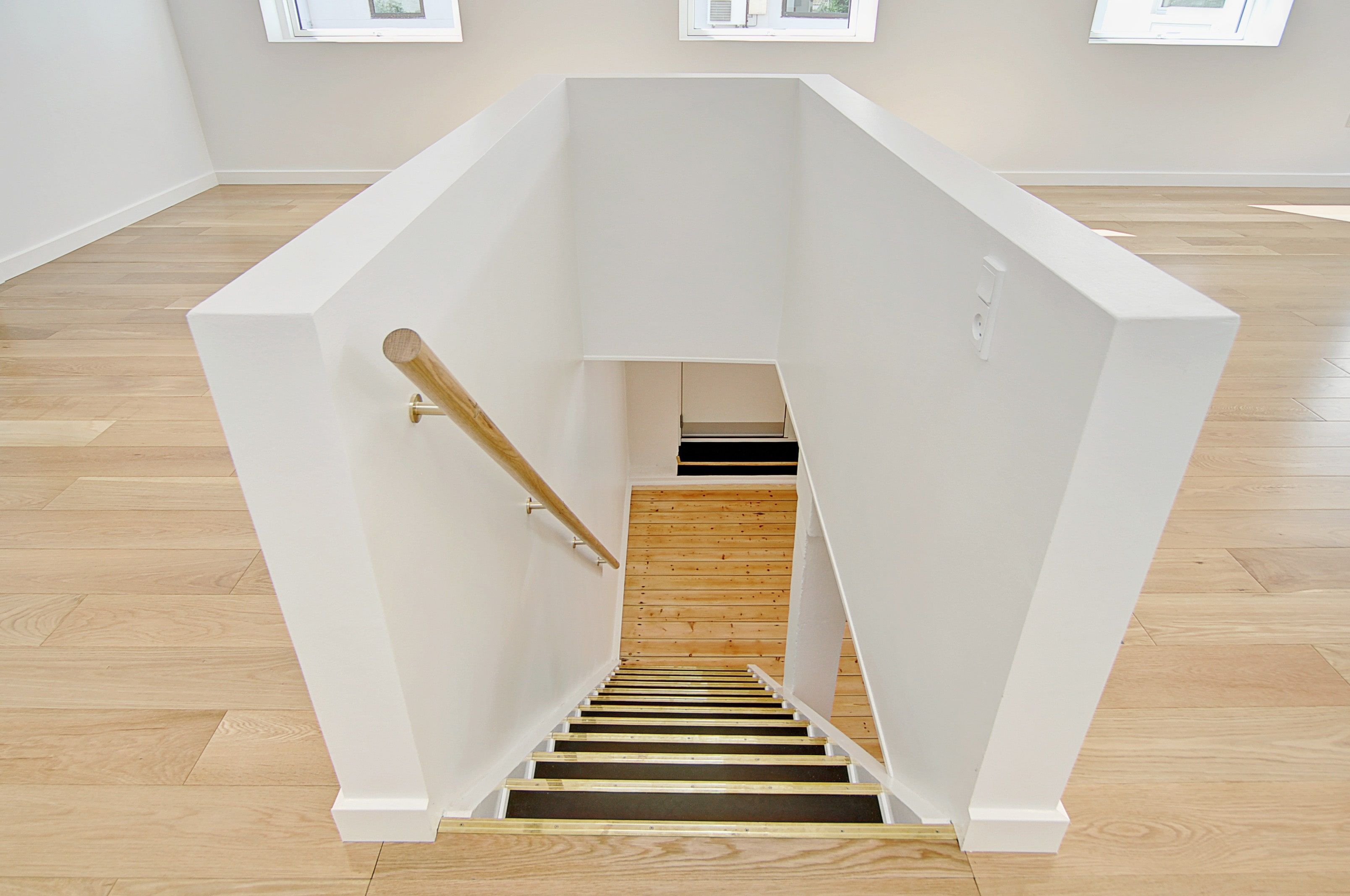 Hvidt vægpanel med trægulve og stige med trætrin og metalgevær. Loftet med træ og hvide vægge og tre vinduer med glas og