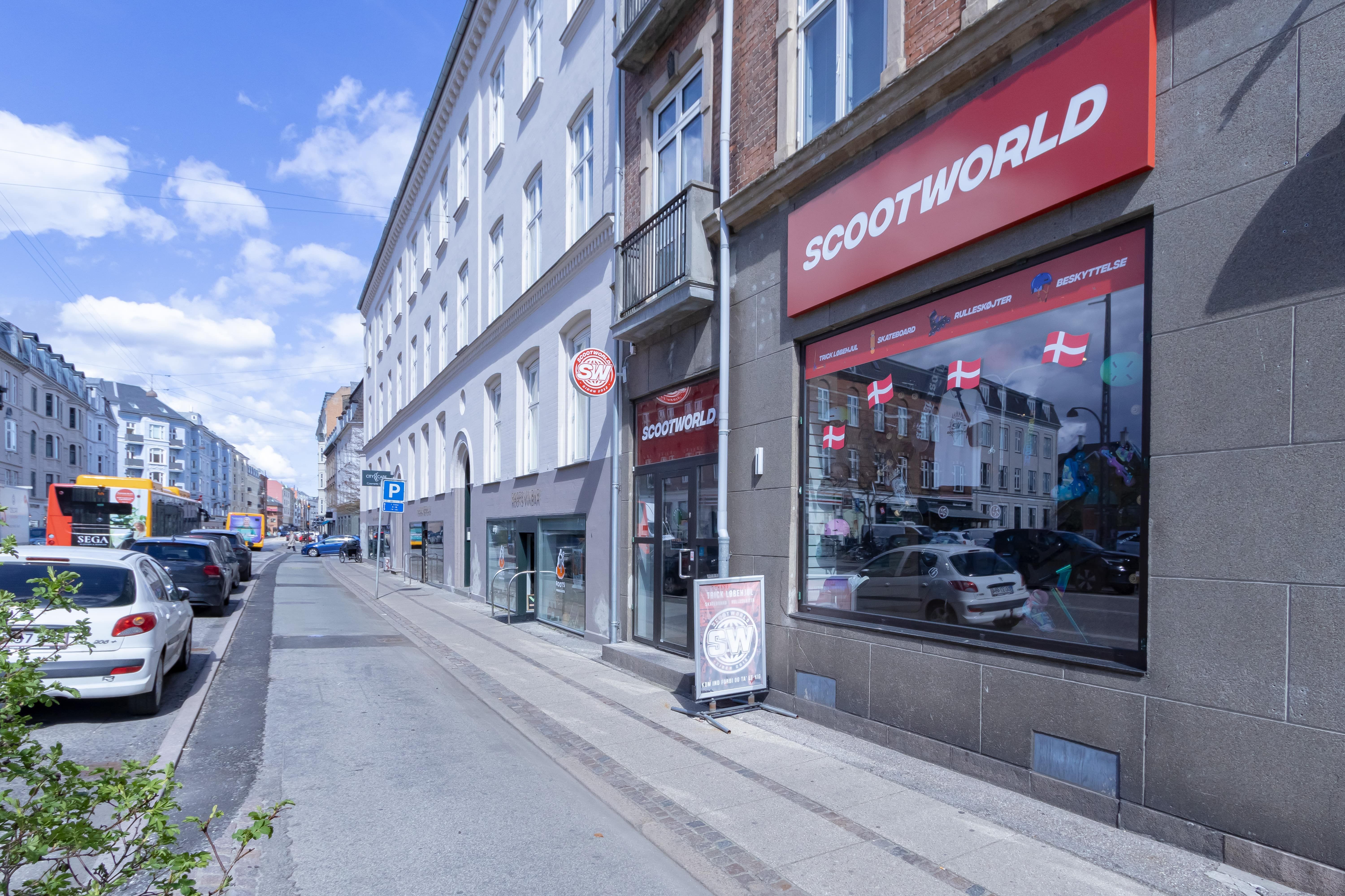 Et butikslokale i byen med en stor rødt og hvidt logo på facaden og mange danske flag i vinduet