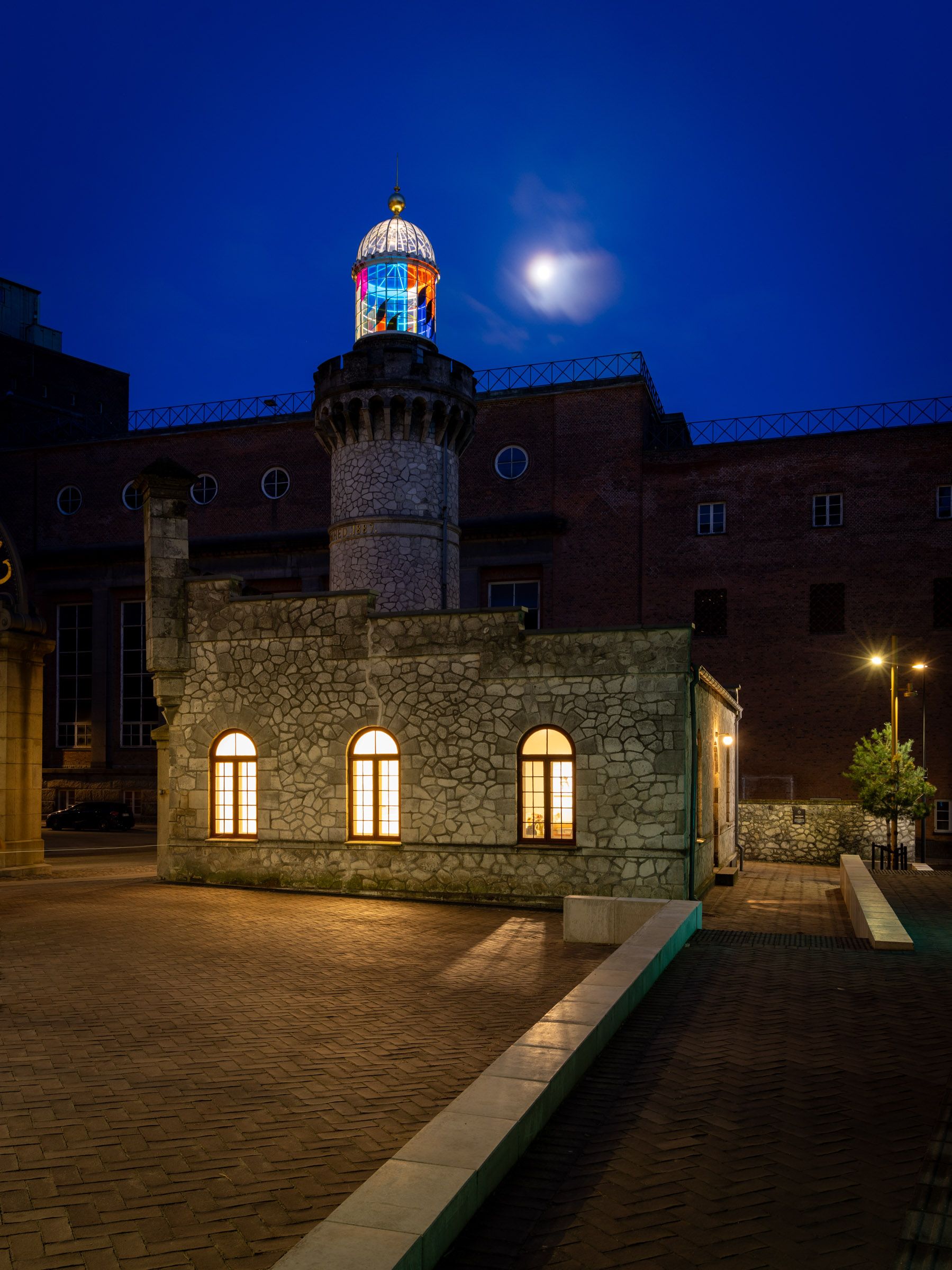 Lyst oplyst bygning med tårn, dekoreret med farverige glasruder og lyse vinduer i en nat med fuldmåne på himlen