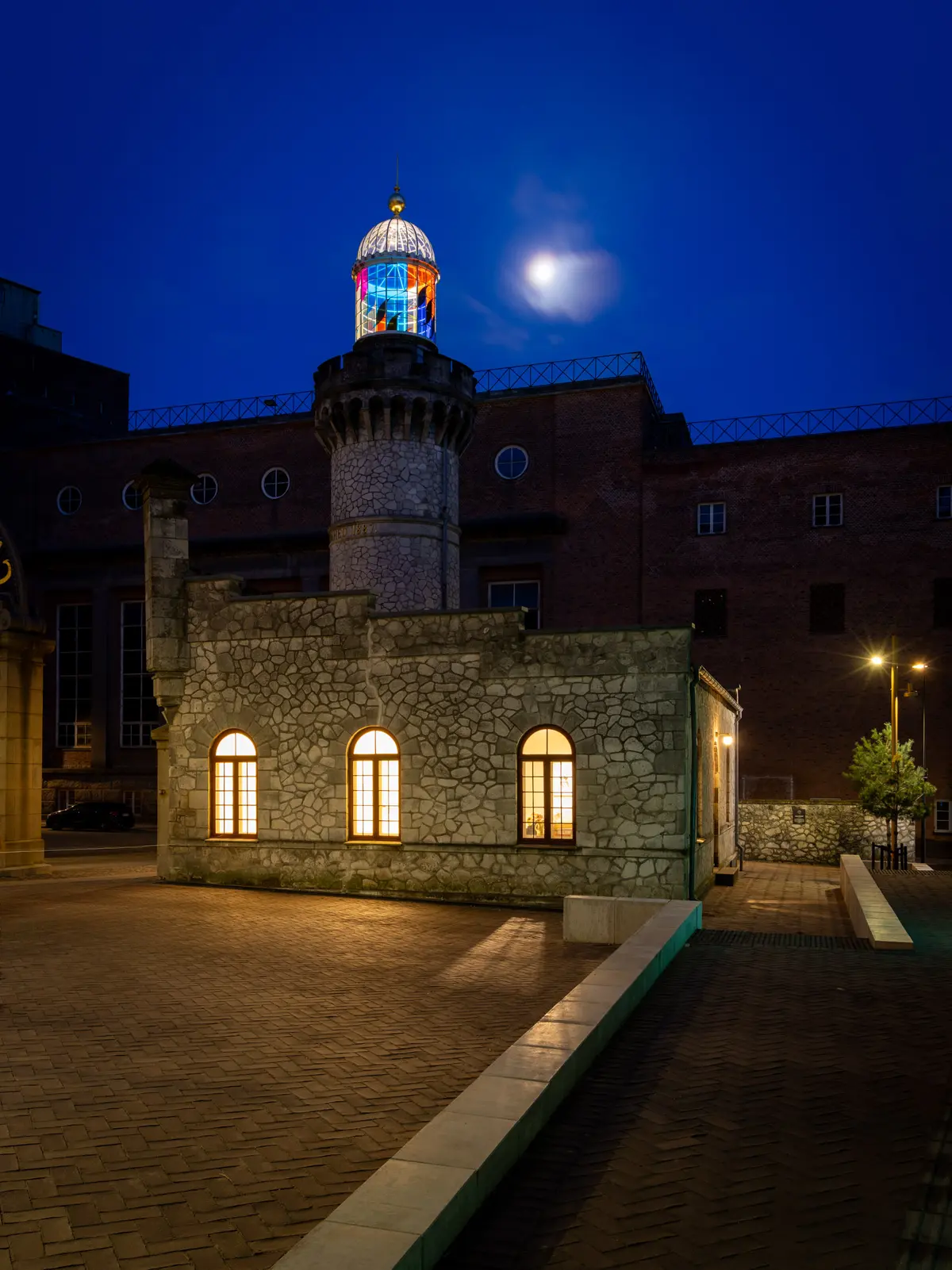 Lyst oplyst bygning med tårn, dekoreret med farverige glasruder og lyse vinduer i en nat med fuldmåne på himlen