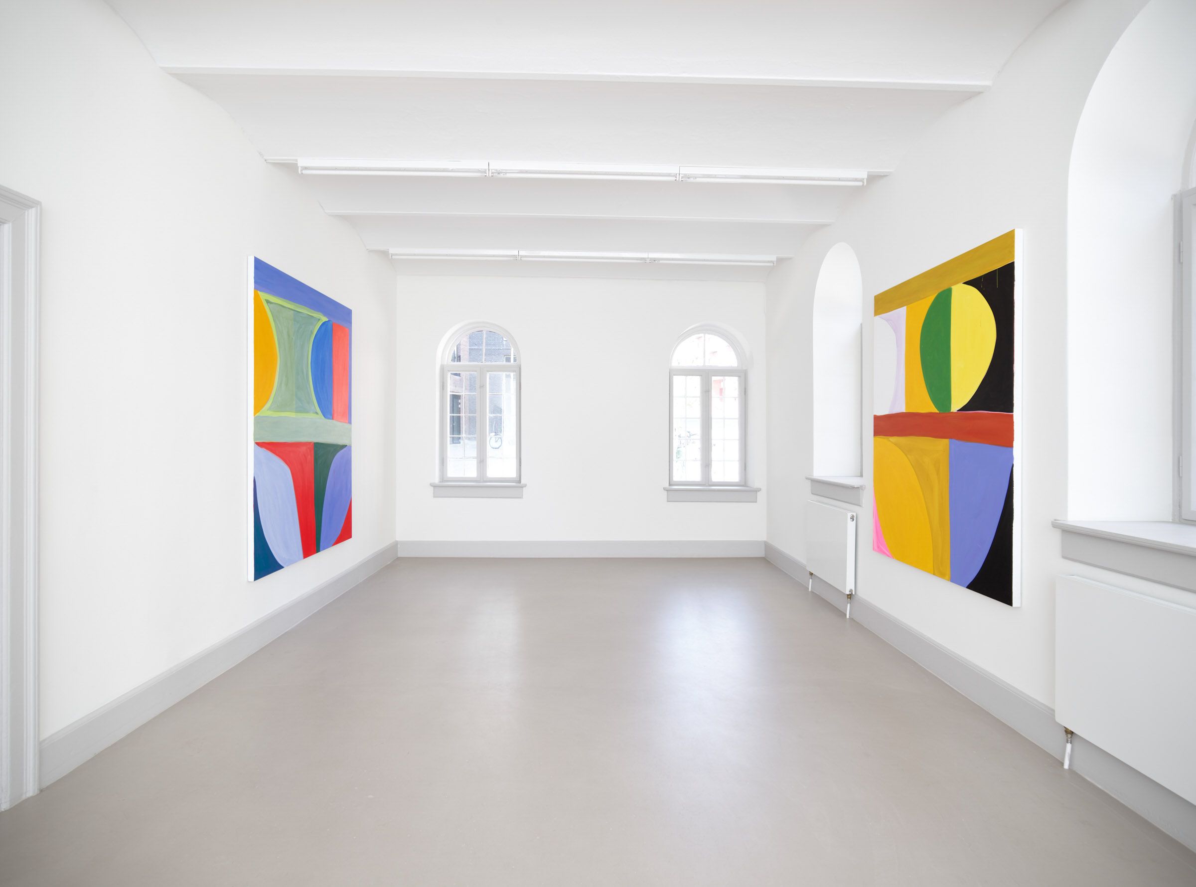 Hvid væg med to store abstrakte malerier og vinduer med udsigt til byen udenfor