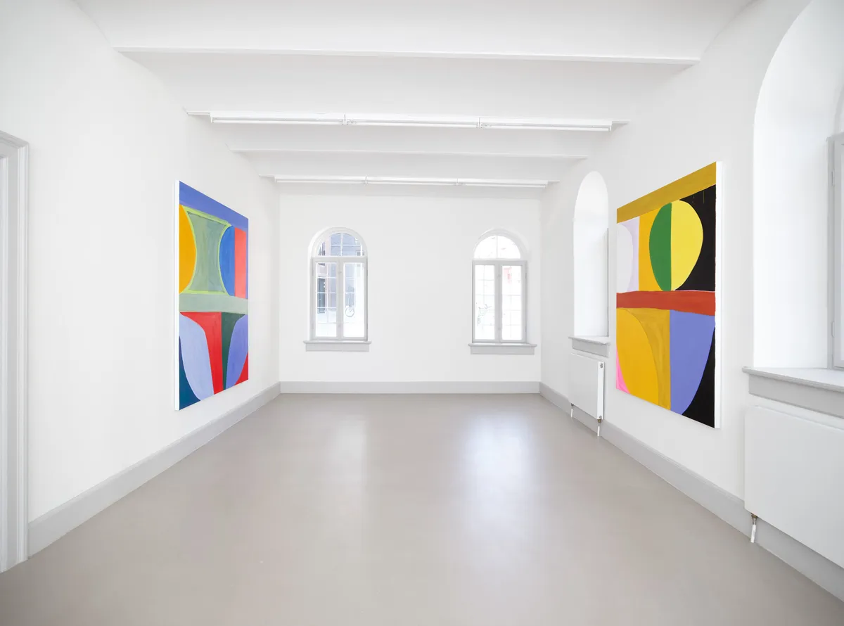 Hvid væg med to store abstrakte malerier og vinduer med udsigt til byen udenfor