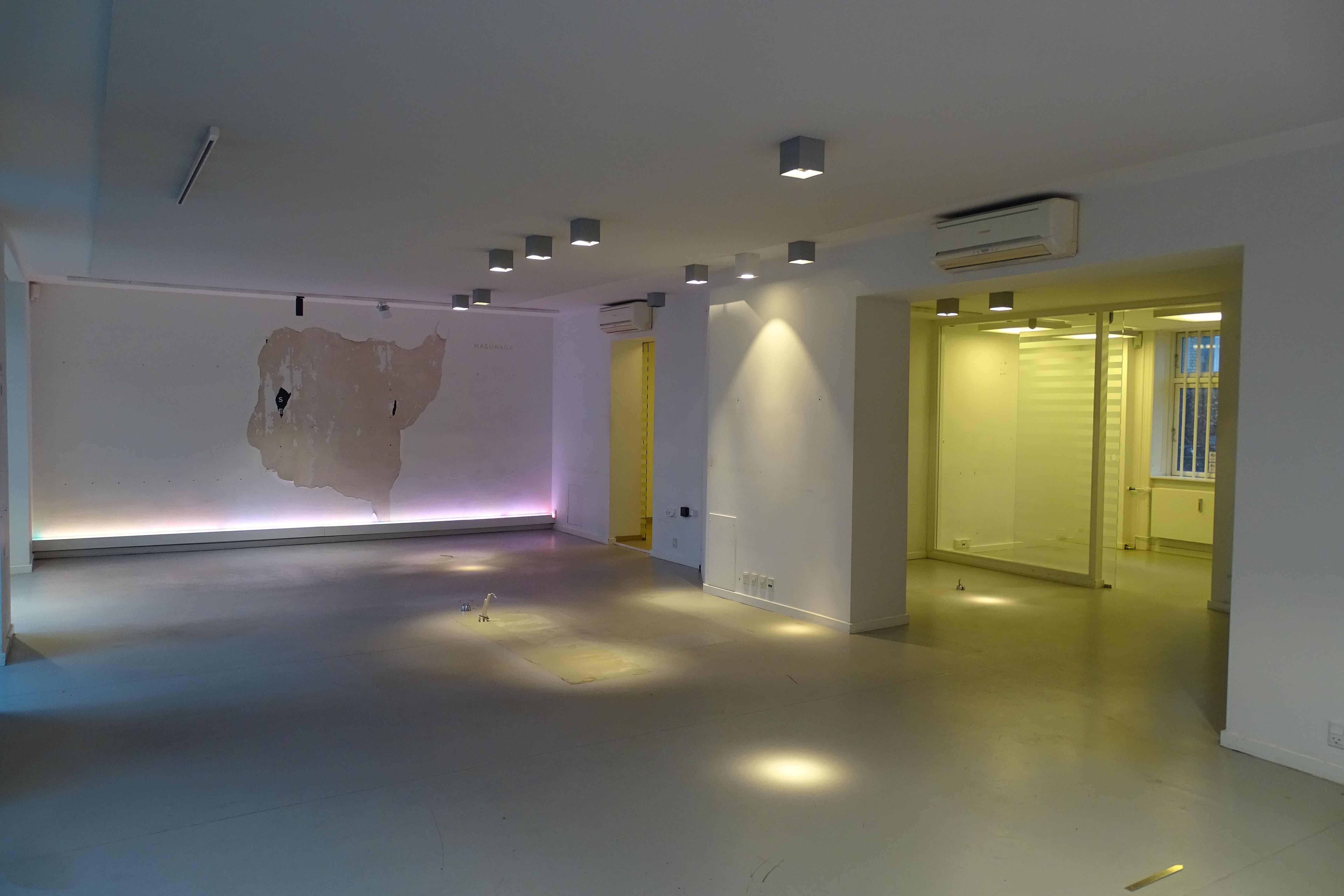 En stor, tom stue med hvide vægge og lysekroner samt et stykke maleri på væggen og luftaffugtere på loftet