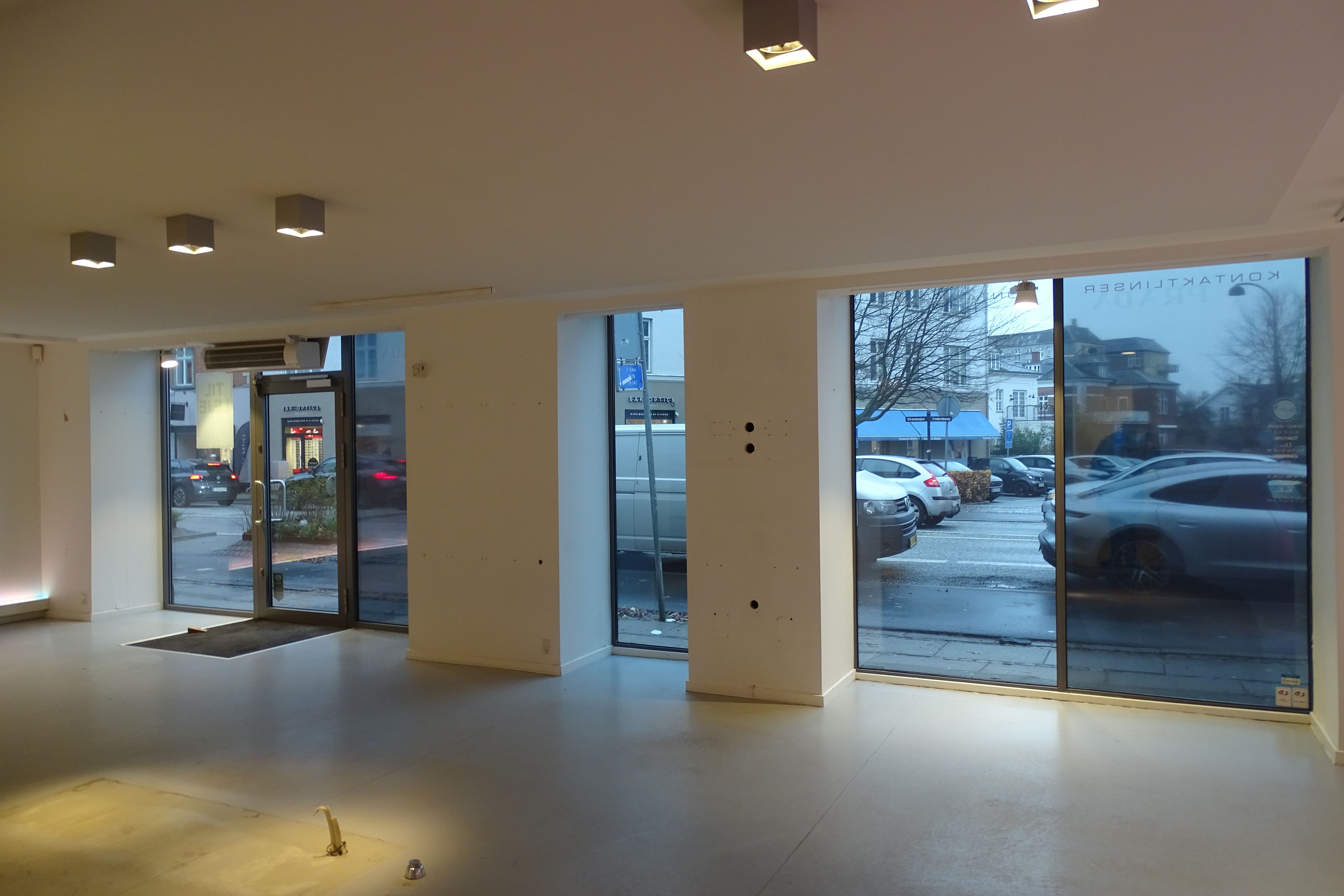 Indenfor et tomt lokale med store glasruder og lysekroner på loftet er der et rødt gulv og to døre med skrift