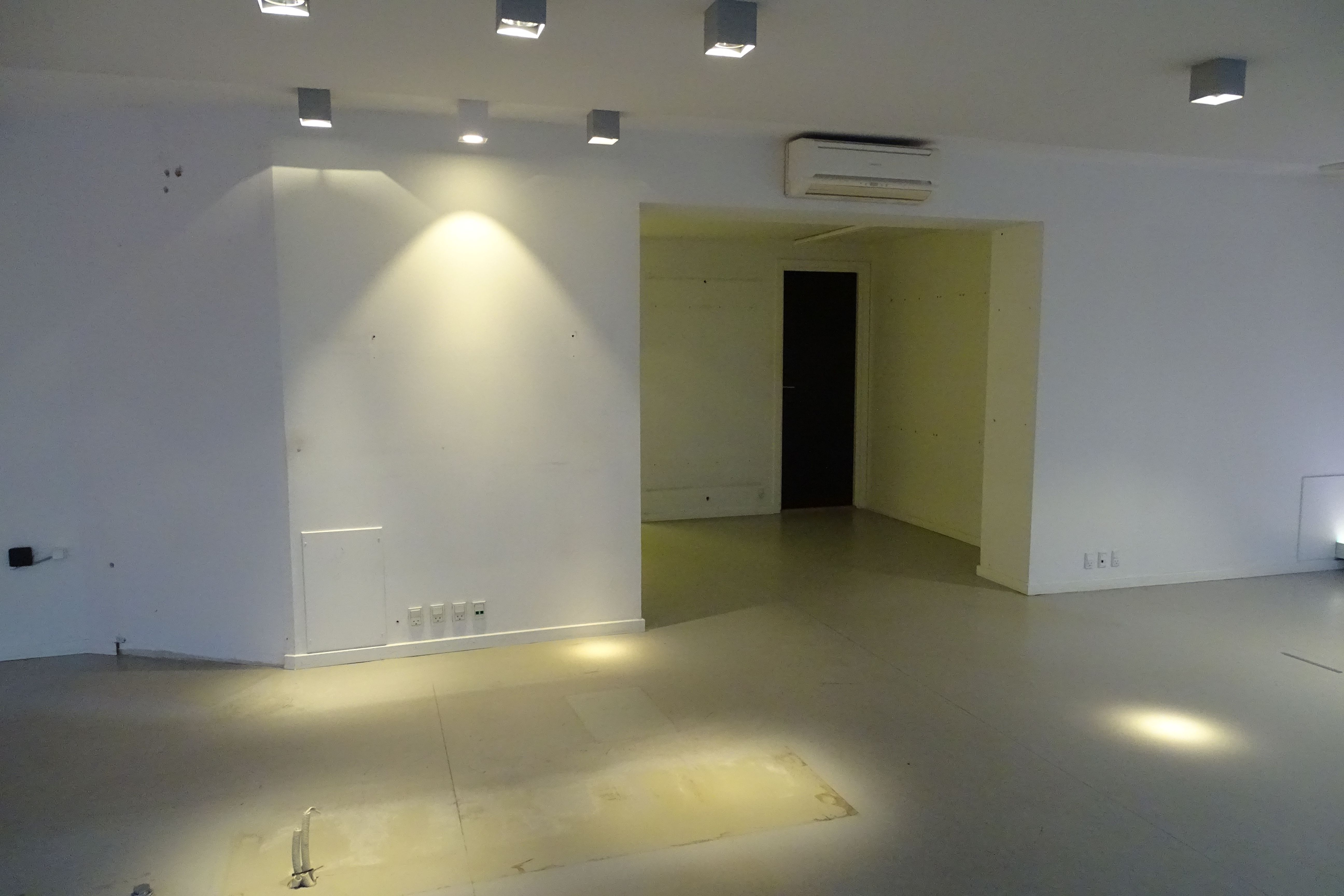 Et rum med hvide vægge og gulv samt en dør, der fører til et rum med et klimaanlæg på loftet og lysepunkter på væggen