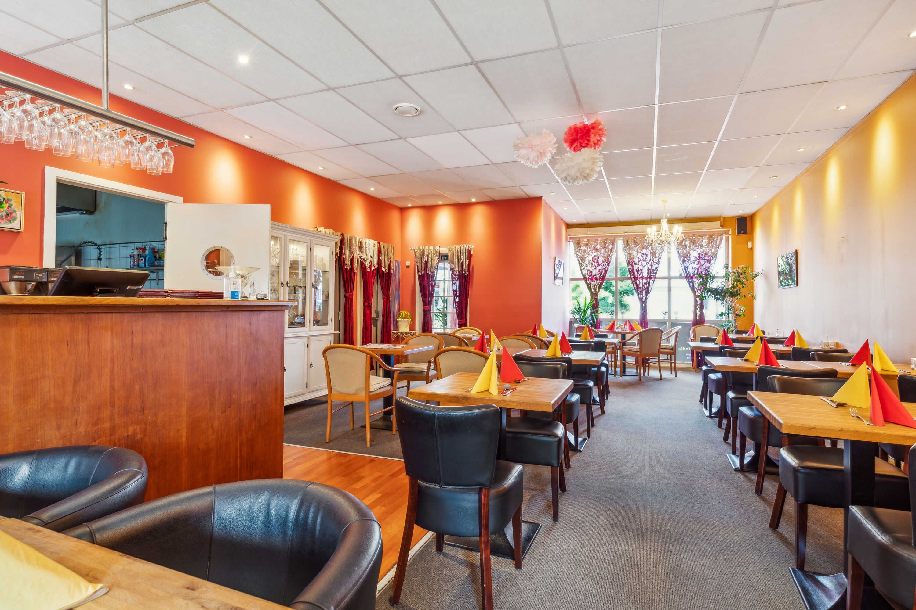 Fusion of India restaurant med orange vægge, hvide loftsplader, lysegult lys, stolpe med vinglas, udstyr, borde, stole,