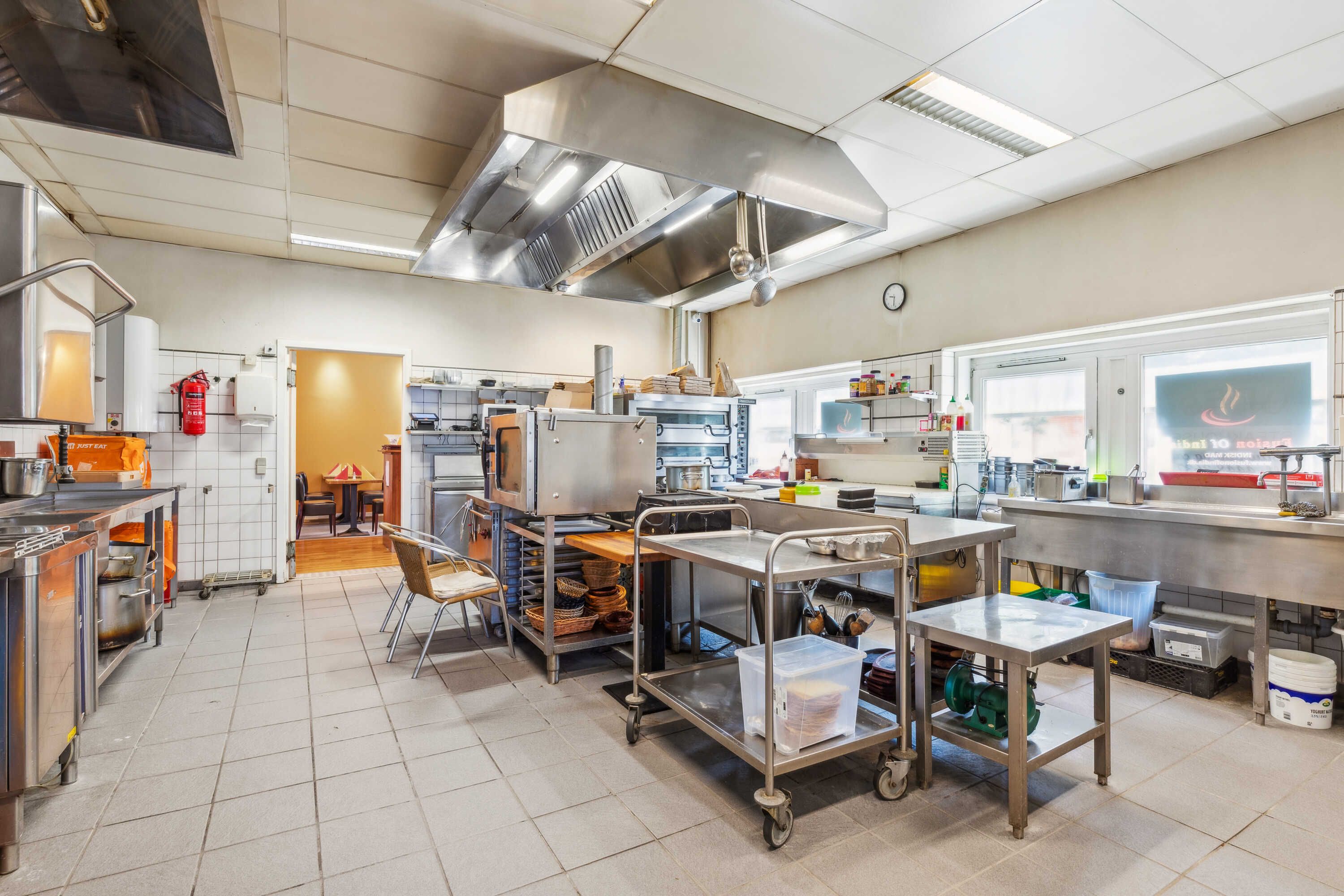 Indretningsfuld kommerciel køkken med flere køleskabe, ovne, komfurer, opvask og flere stålvogne.
