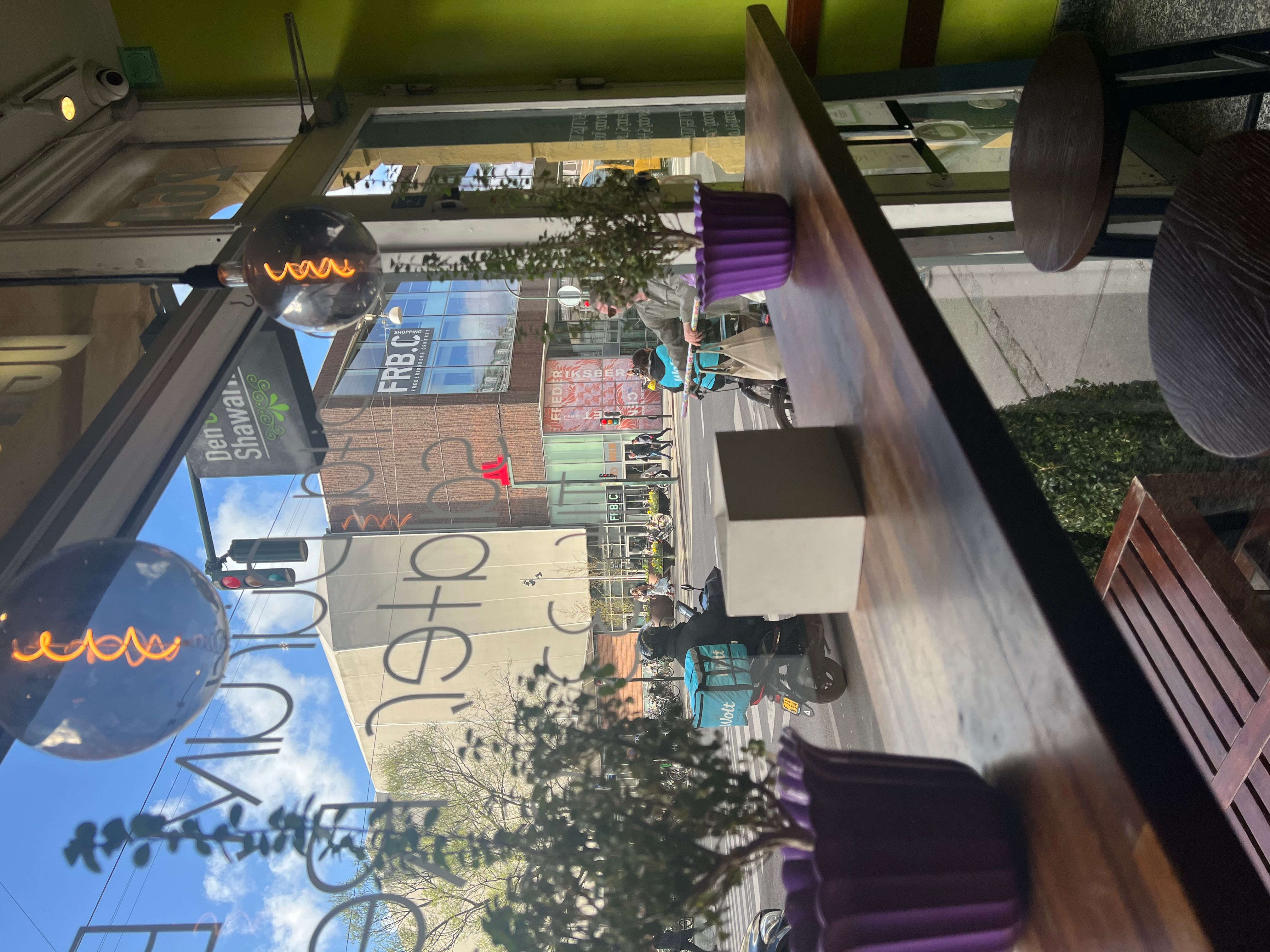 Inde i et café med bord og stole, hvor to lysekroner med varme farver er hængt op og en sofa i hjørnet