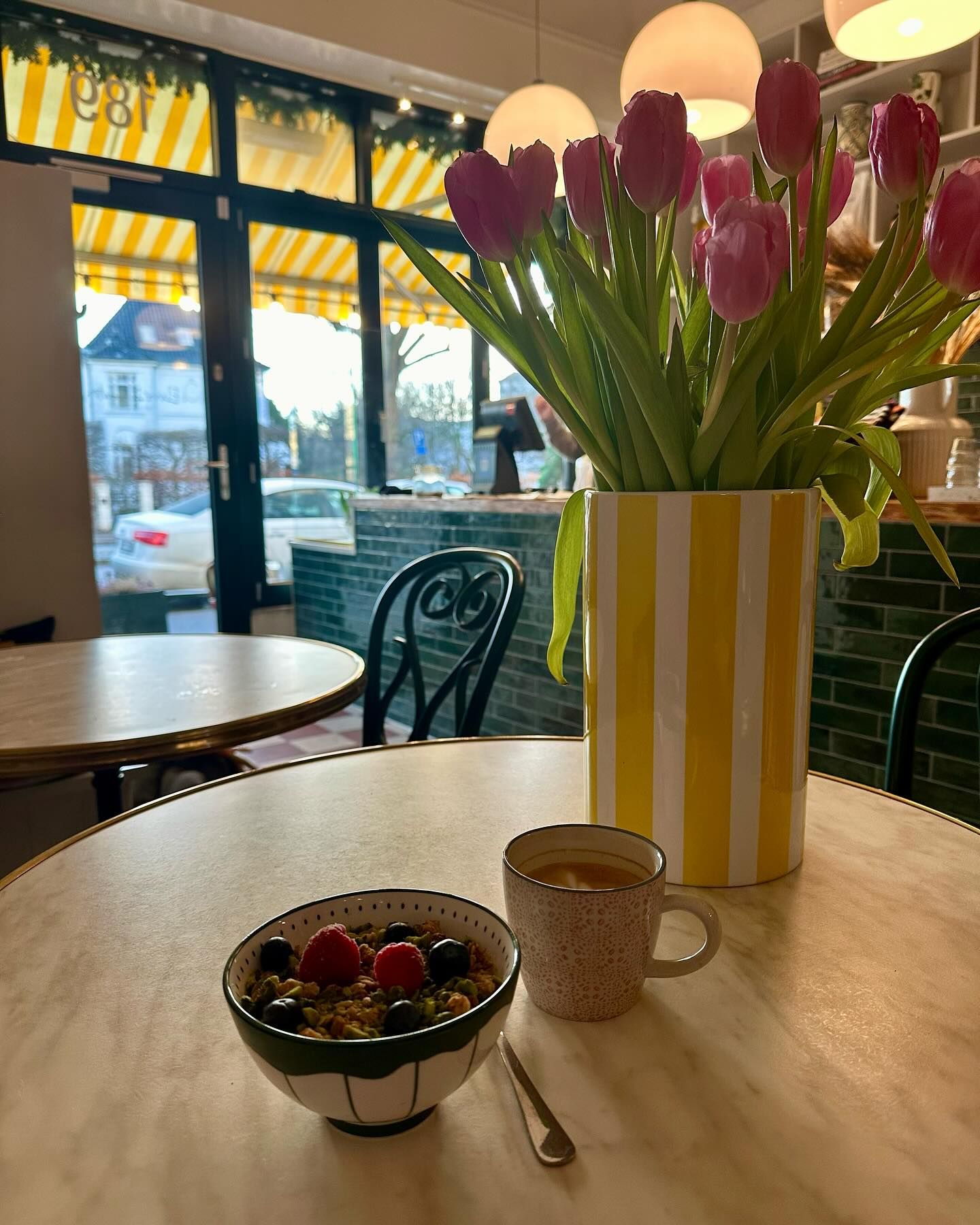 En rund bord med et glas med krydret korn og bær og en kop varm drikke, samt en vase med tulipaner og en baggrund med en