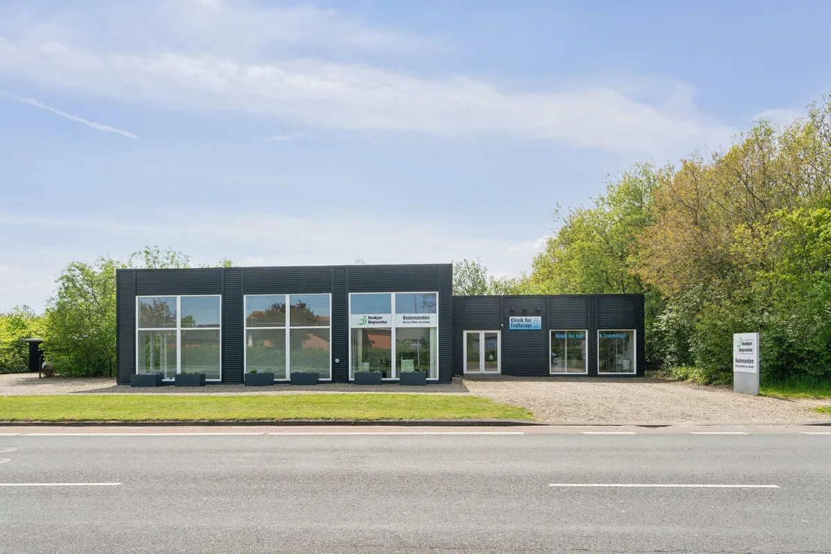 Erhvervslokale med indgang og vinduer, udstyret med tekøkken og have. Tegn: Klinik for Fodterapi. Bygningen har sort facade