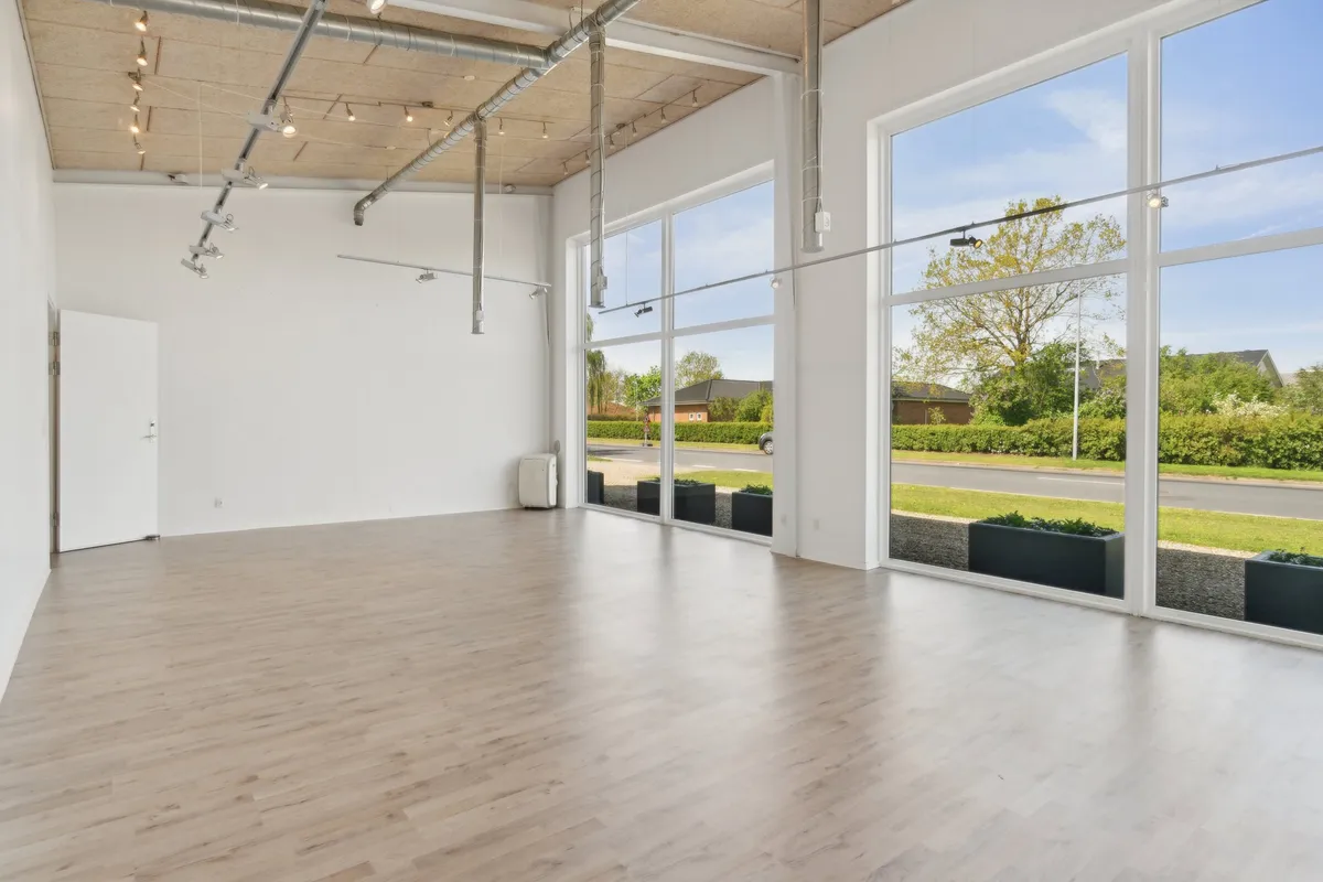 Ingen møbler, kun lyse gulve og store vinduer i lokale med slanke metalprofiler og lysepunkter i loftet