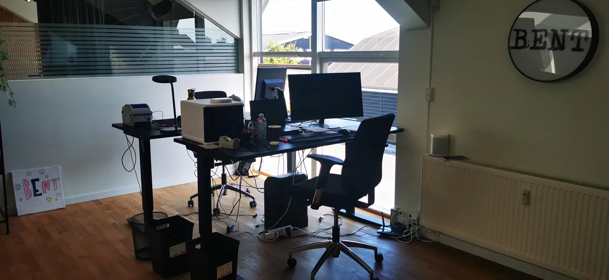 Kontor med skrivebord og flere skærme og skrivebordslamper og ståbord og radiatorer og tekstplakater og runde mærkeskilte