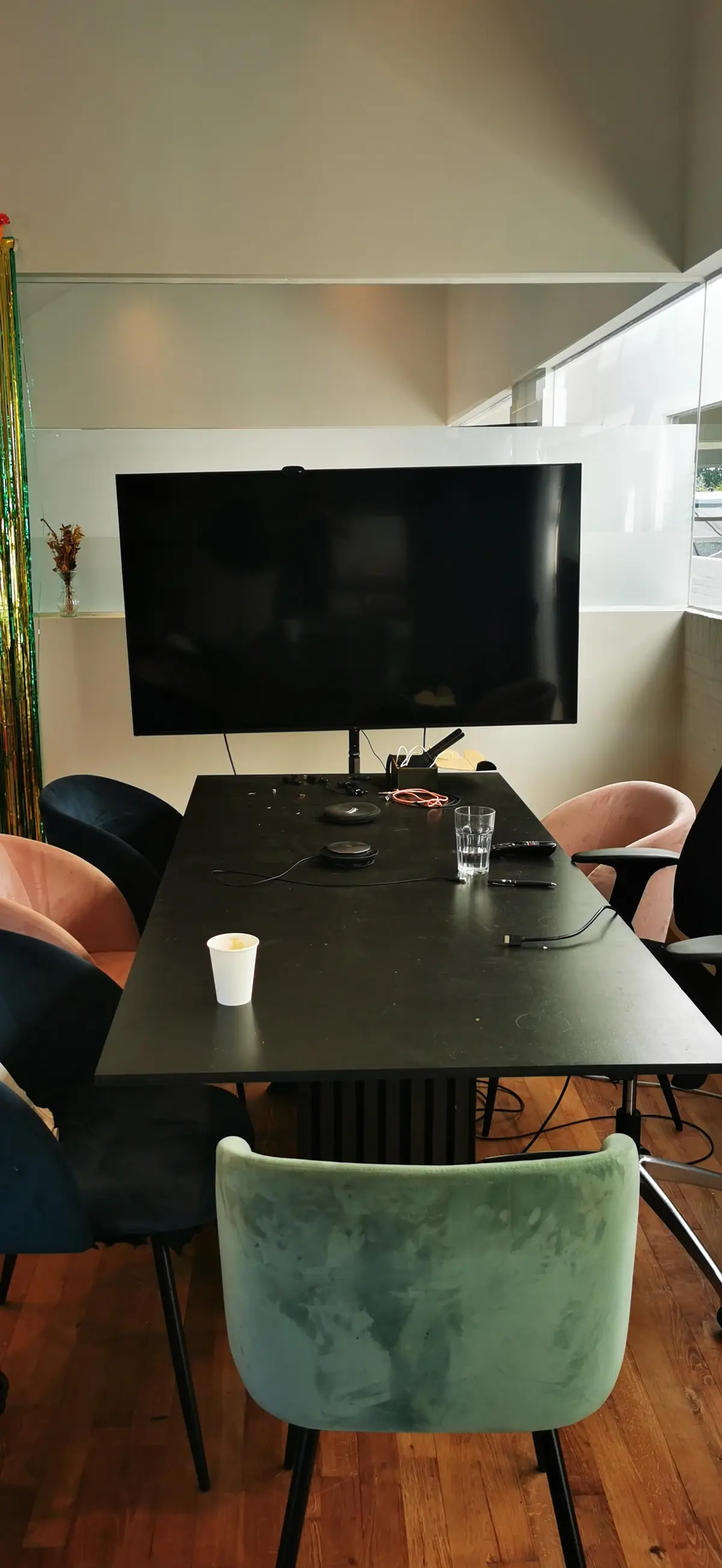 Kontorrum med skrivebord, tv, og mødestol med kuffert. I baggrunden står en vase med tørrede blomster.