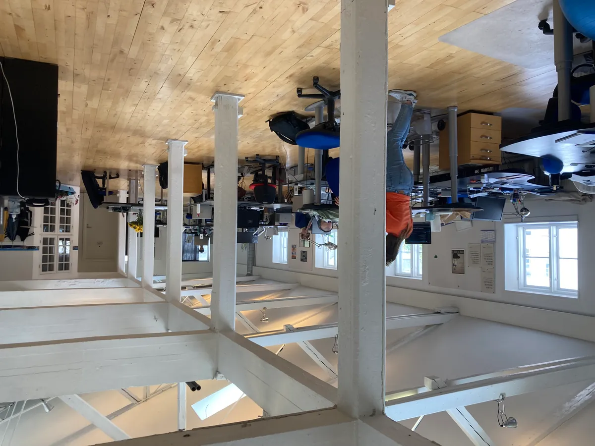 Kontorloft med høje hvide bjælker og en kvinde i orangebukser hængende i loftet med en person under hende på gulvet