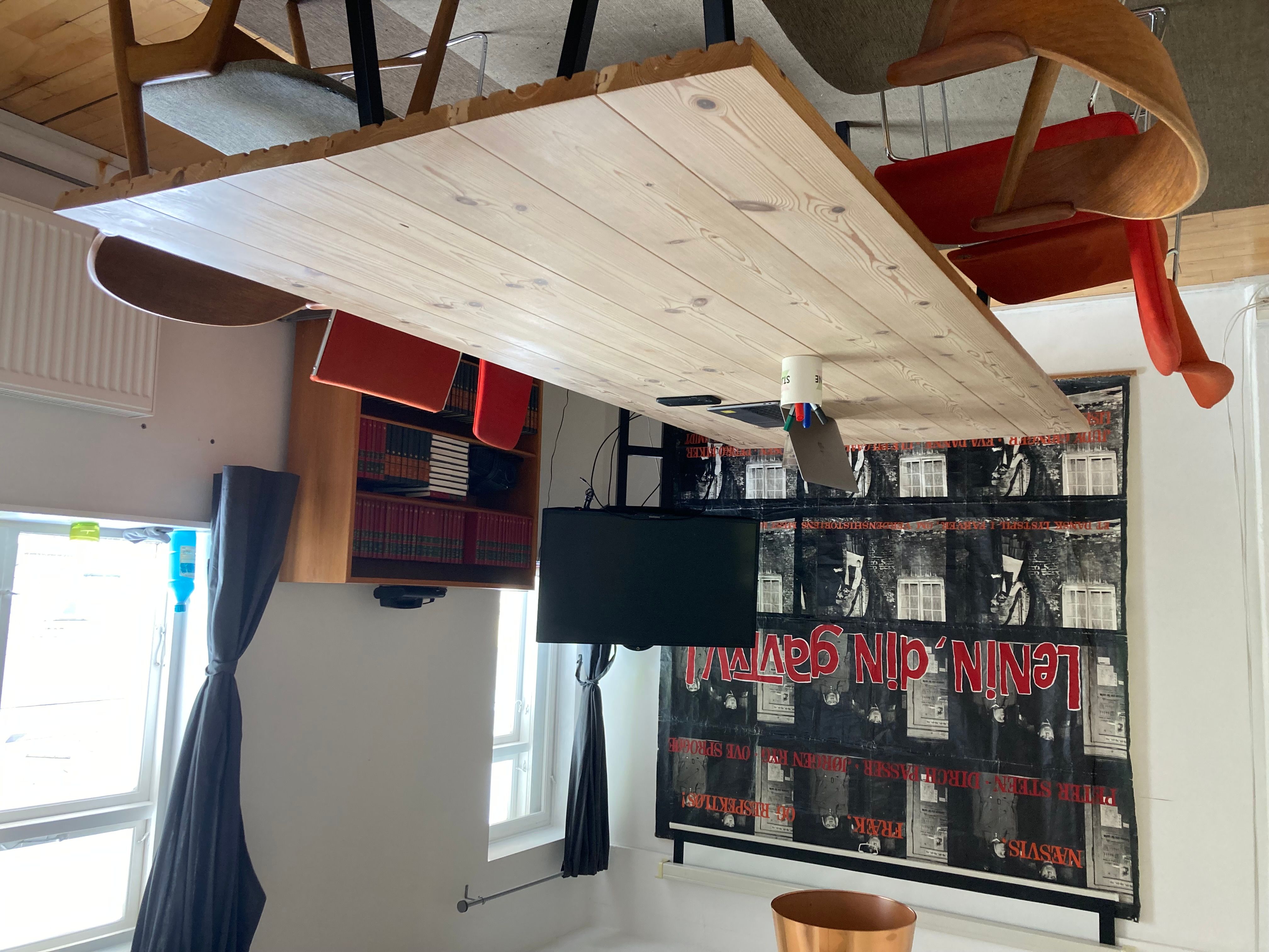 Kontor med loftsbord, tv, skrivebord, skrivebordslamper og stol samt skrift på væggen