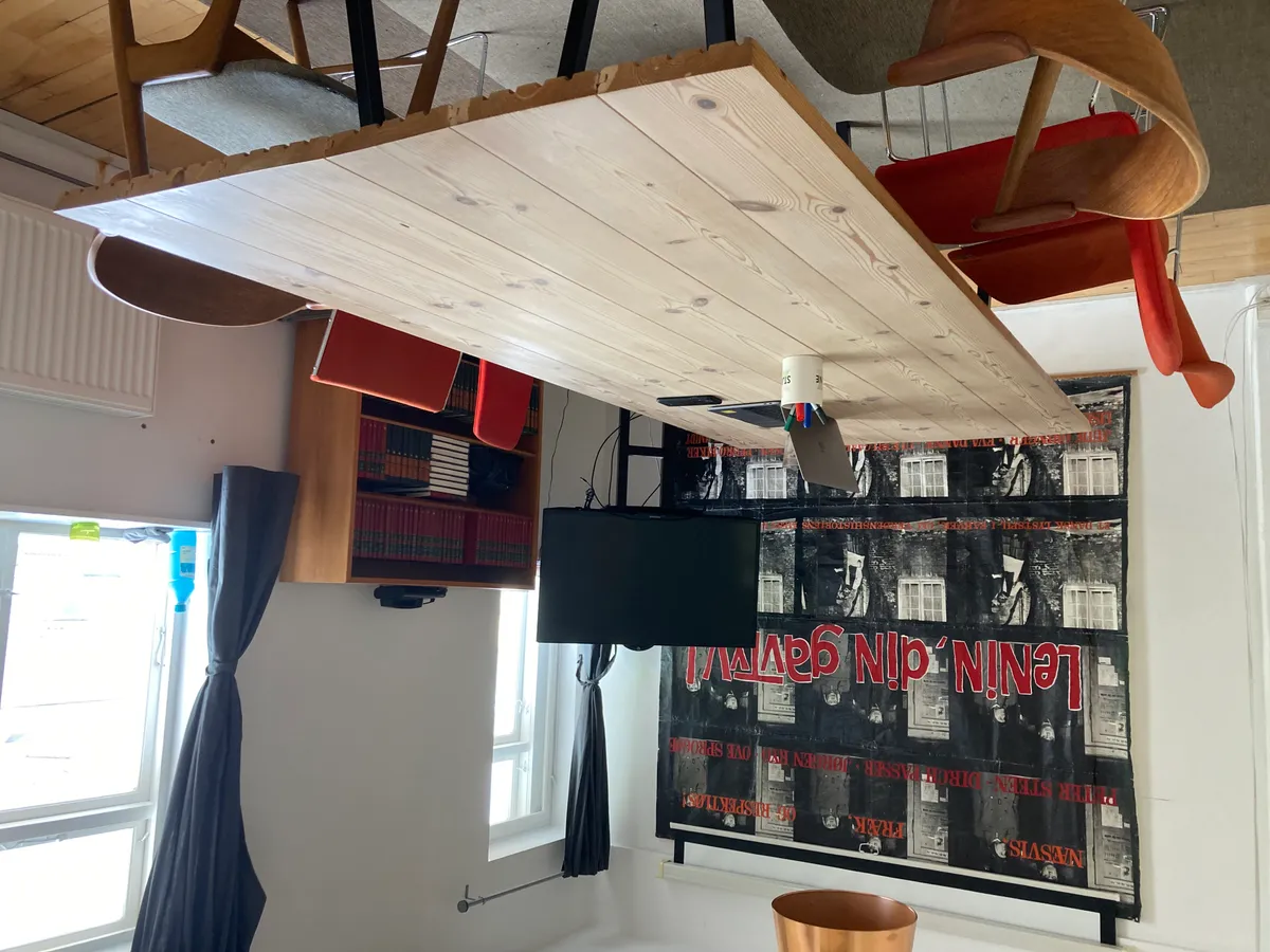 Kontor med loftsbord, tv, skrivebord, skrivebordslamper og stol samt skrift på væggen