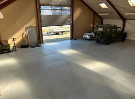 Garage med åben dør og to biler parkeret i garagen og trailer parkeret udenfor