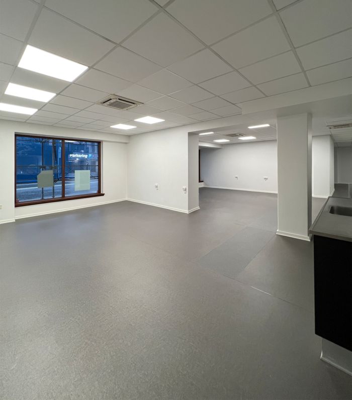 Et glasvinduesudsnit med reklametekst. Et rum med lys gulvbelægning og hvide vægge. To hvide søjler i baggrunden. To hvide