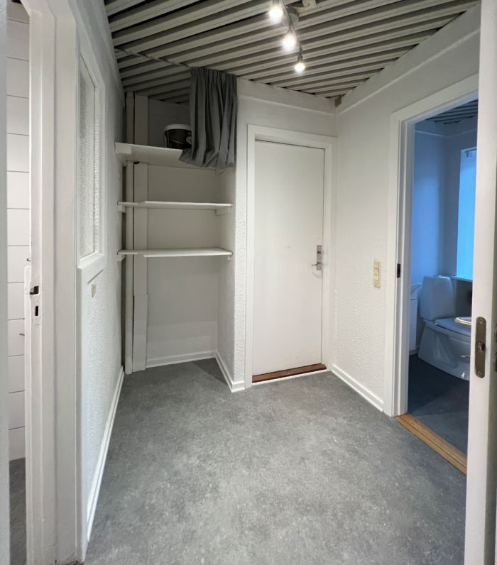 Lejemål med højloft og hvide vægge, moderne indretning, åbne døre og et badeværelse med toilet og lys