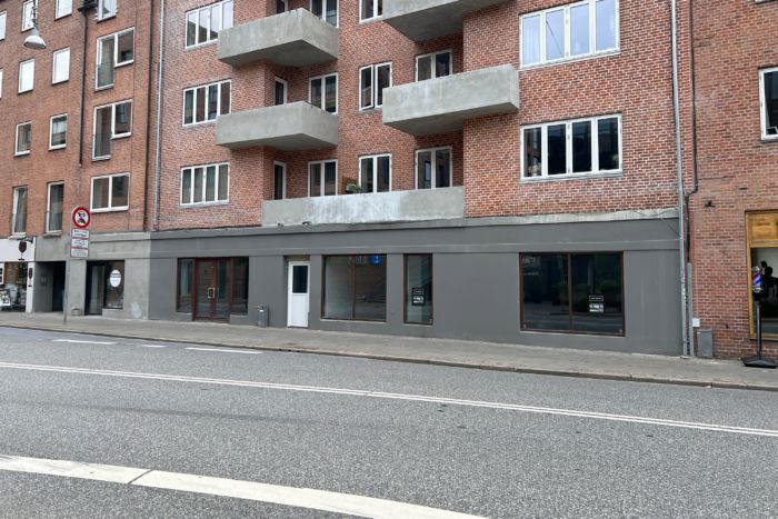 Lys og moderne lejemål med vinduer og døre på en tom gade i et område med mange bygninger og butikker