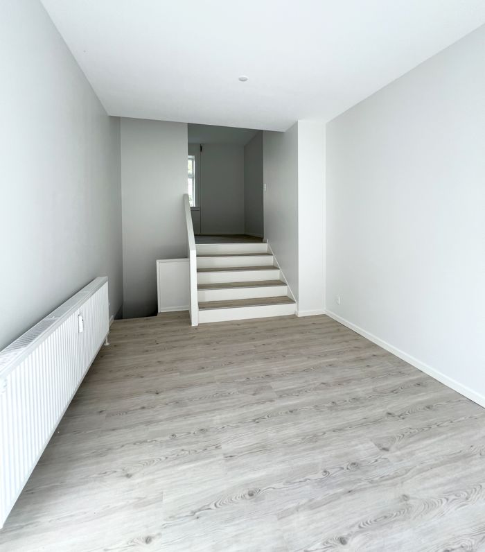 Ny lejlighed med lyse gulve og hvide vægge, samt trappe og dør. Ingen møbler, men radiator og moderne design. Perfekt til