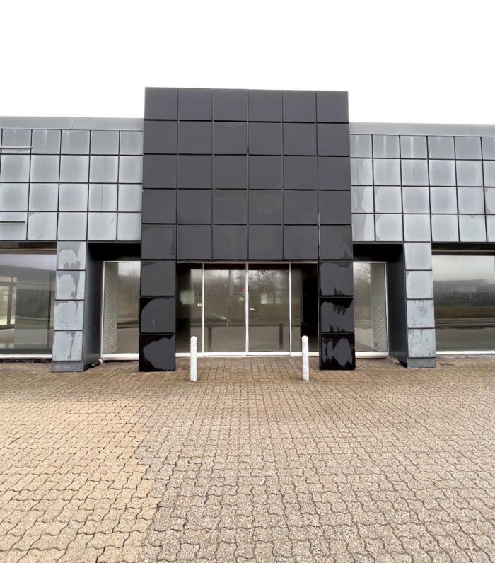 Moderne bygning med sort facade og glasvinduer og indgangsparti med hvide søjler og brolægning foran