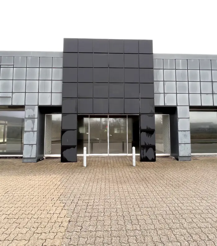 Moderne bygning med sort facade og glasvinduer og indgangsparti med hvide søjler og brolægning foran