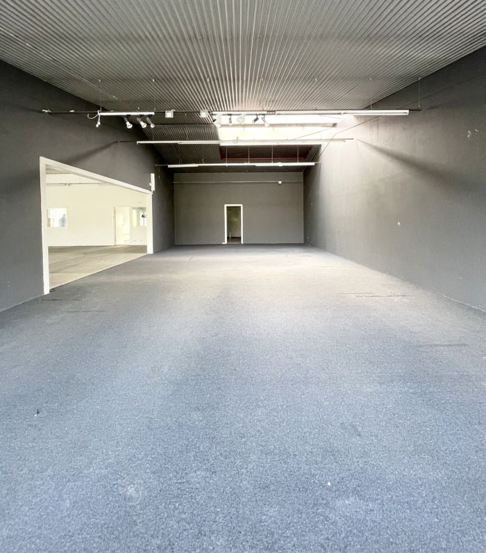 Stor lejeområde med højloft og lyse loftslampe. Hvid og grå indretning med to lyse døre. Gulvet er dækket med lysegrå