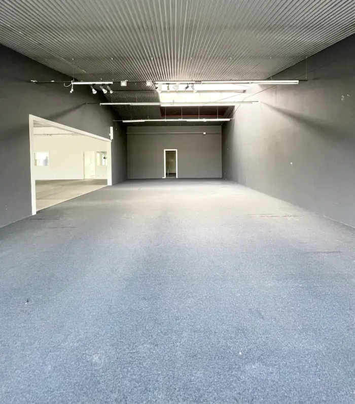 Stor lejeområde med højloft og lyse loftslampe. Hvid og grå indretning med to lyse døre. Gulvet er dækket med lysegrå