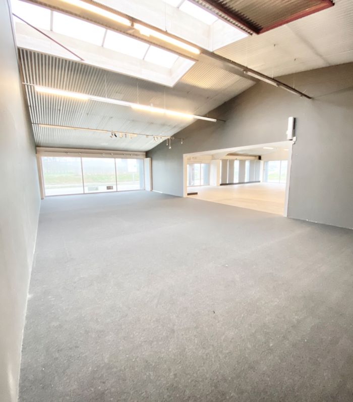 En stor, tom, industriel hall med højt loft, store vinduer og lyse gulve, hvor der er installeret store lysekroner