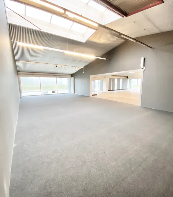 En stor, tom, industriel hall med højt loft, store vinduer og lyse gulve, hvor der er installeret store lysekroner