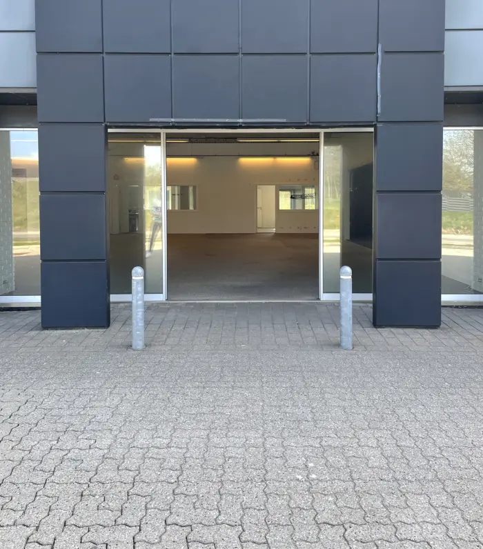 En nybygget butikslokal i Hjørring med en moderne facade og åbne glasdøre med poler og en indvendig gulvbelægning.