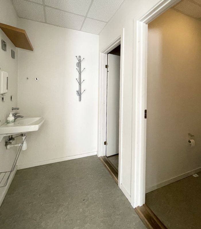 Et moderne badeværelse med hvidt loft, hvid væg og gulv samt en hængekrog med flere kroge og en håndvask med sæbe