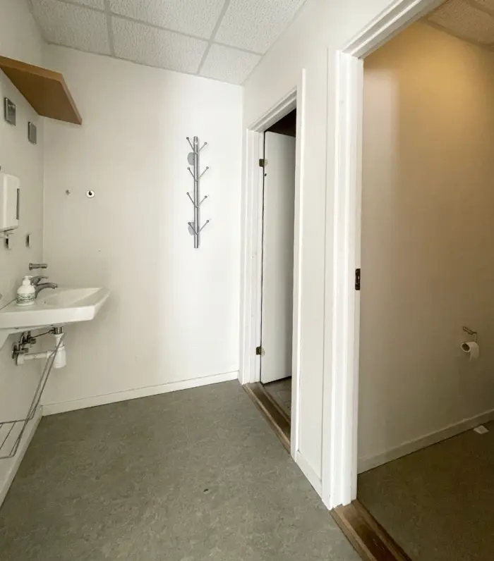 Et moderne badeværelse med hvidt loft, hvid væg og gulv samt en hængekrog med flere kroge og en håndvask med sæbe