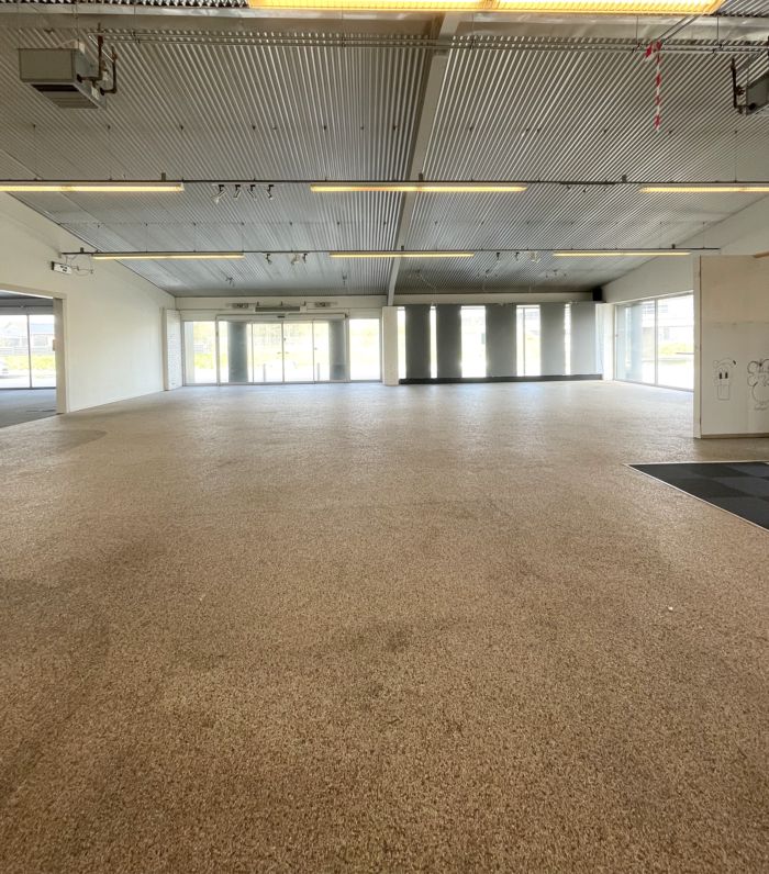 Store tomme lokaler med karpetgulv og hvide vægge, store vinduer og to store døre i baggrunden