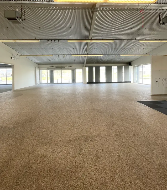 Store tomme lokaler med karpetgulv og hvide vægge, store vinduer og to store døre i baggrunden