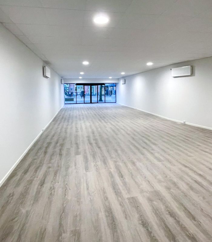En tom, hvid malet kontorlokal med lyse gulvbelægning og flere indbygget klimaanlæg i loftet. Lysepunkter er indbyggede i