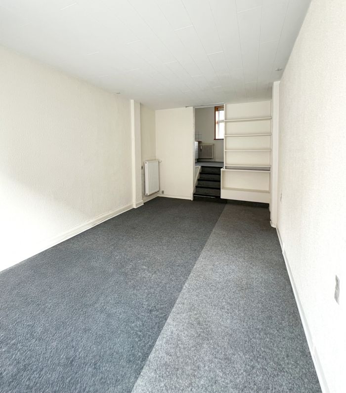 Lejlighed med lysegult loft og vægge, mørkegult gulv og et hjørneskab med to hvide hylder i en hjørne.