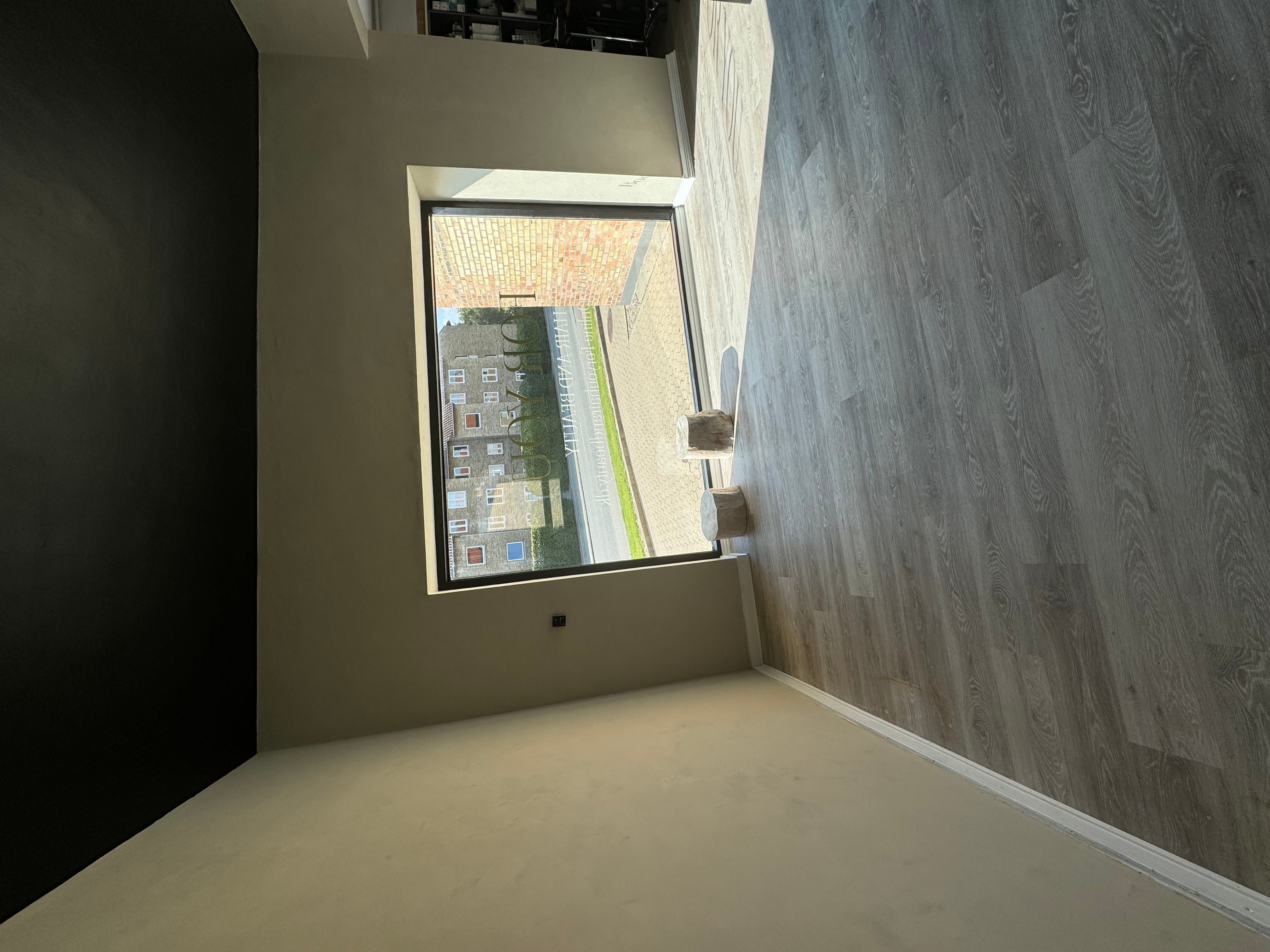 En stor vinduesfløj og lysegul gulvbelægning i en tom frisørsalon med mørke vægge og et vindue til gaden