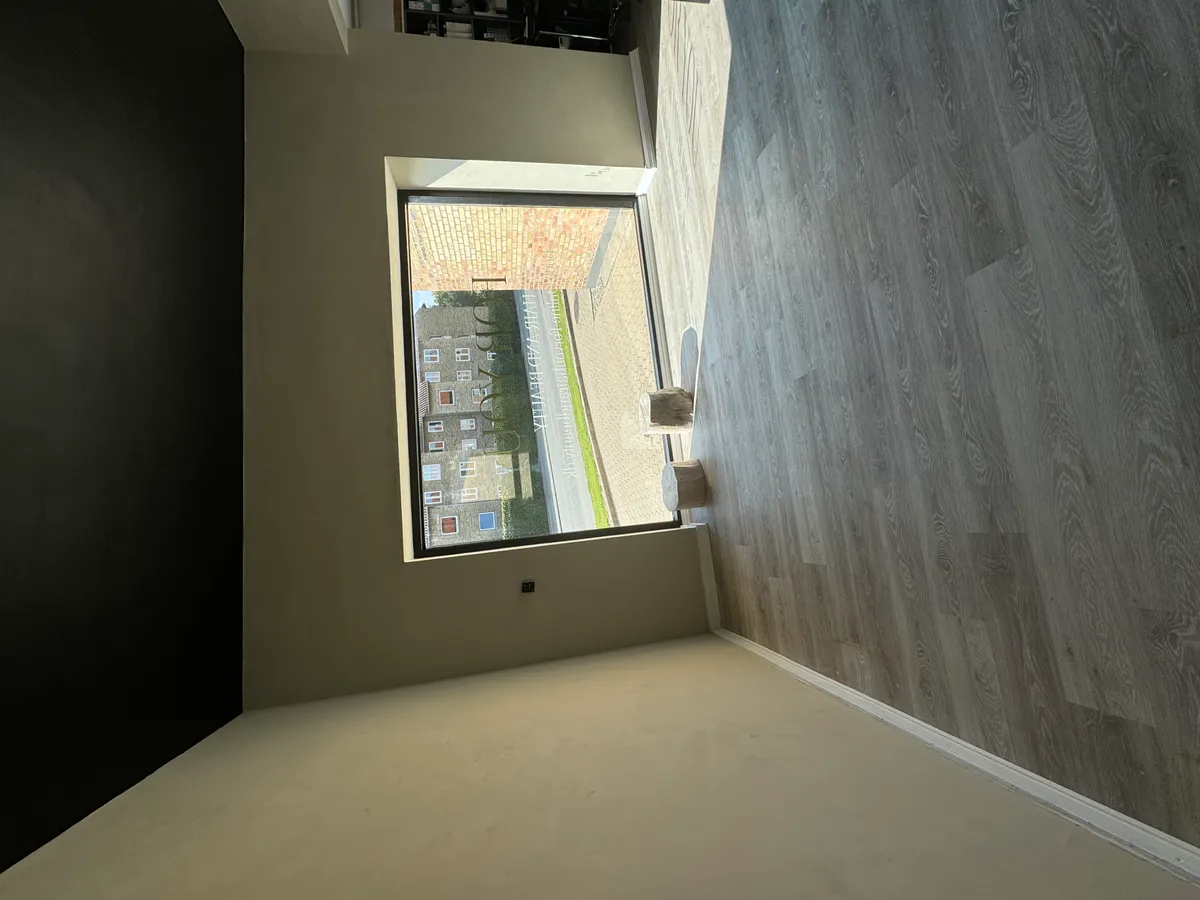 En stor vinduesfløj og lysegul gulvbelægning i en tom frisørsalon med mørke vægge og et vindue til gaden