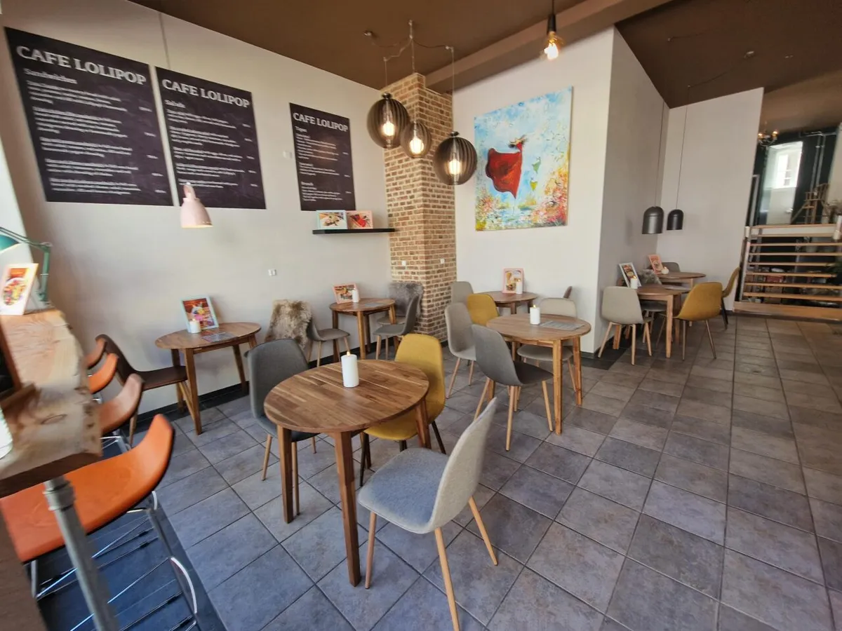 Et lille café med små runde borde og stole med lyse farver og et maleri på væggen