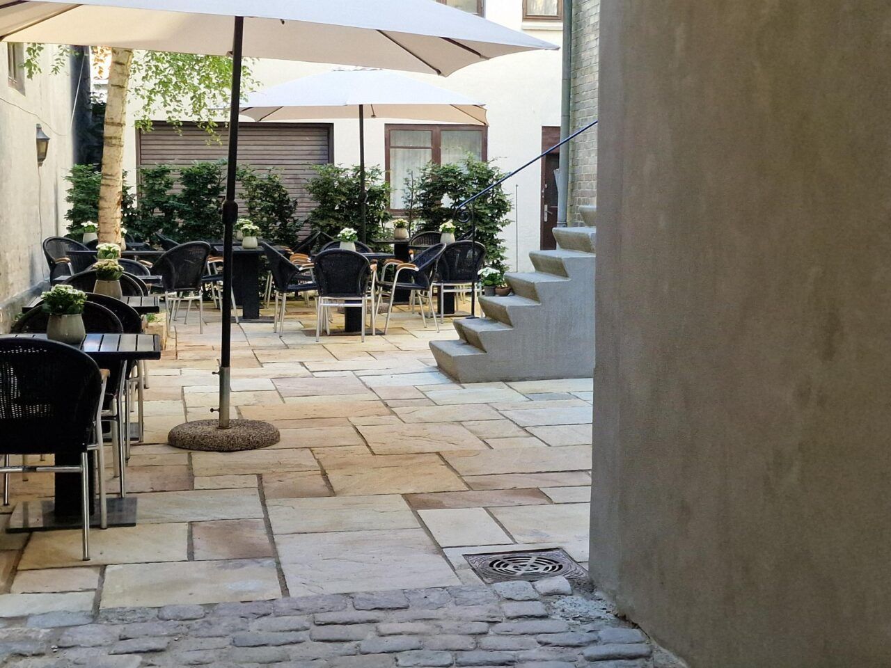 Have med grønne planter og buer samt bord og stole, hvor der er blomster i vaserne