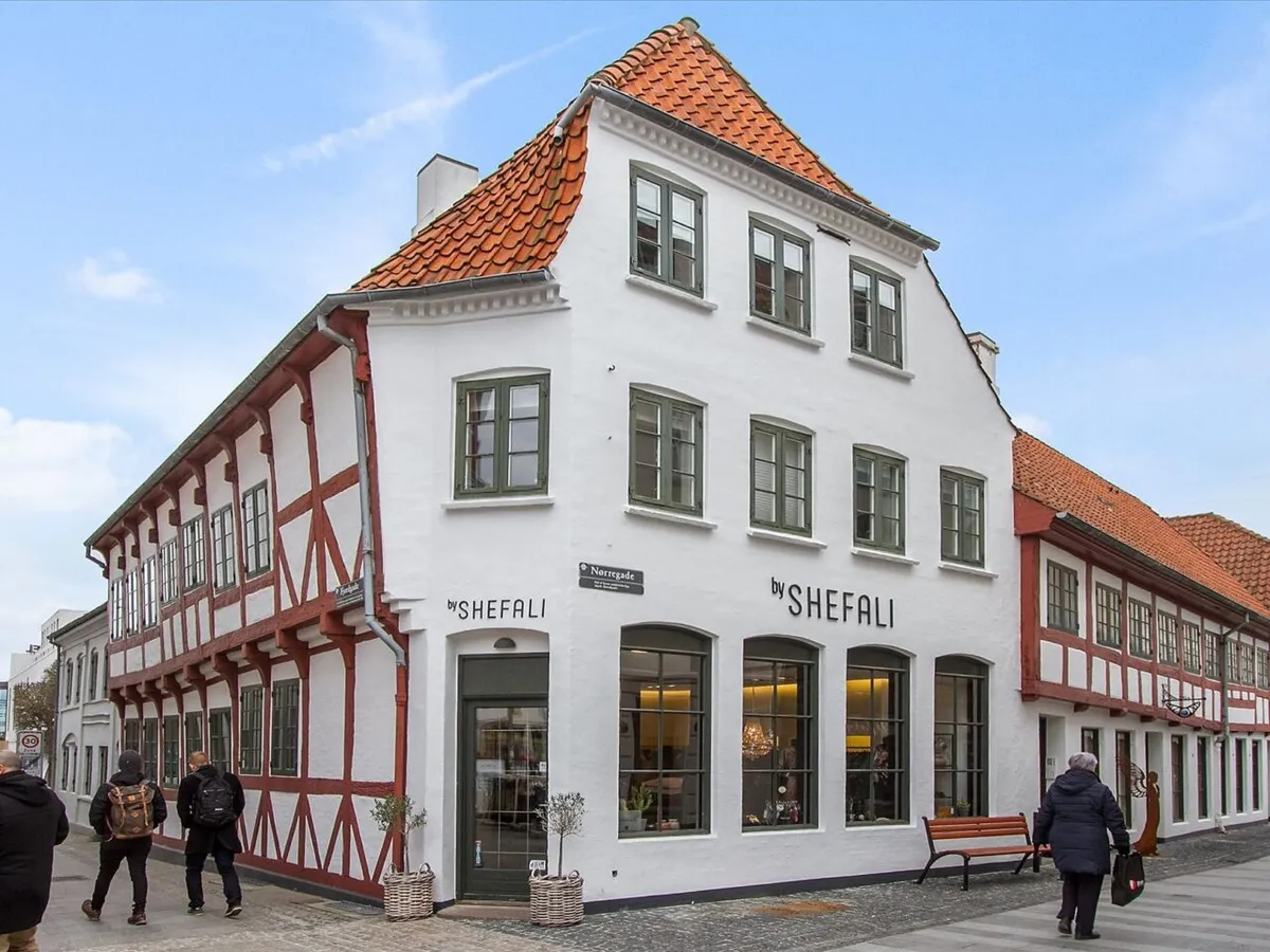 På hjørnet af Nørregade og Bredegade Torv ligger en butik med røde tag og hvide vægge og vinduer, sammen med gående