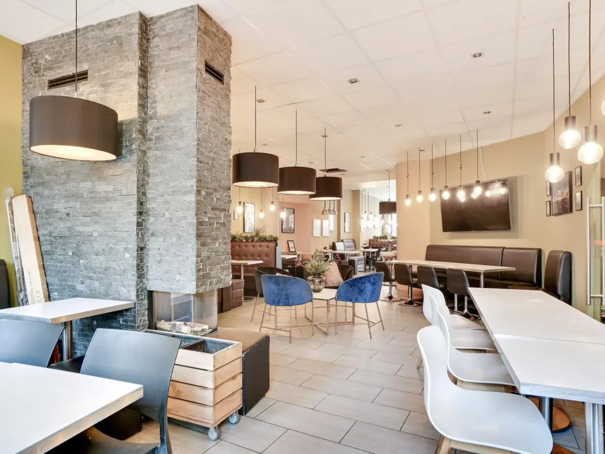 Et moderne kafé med lyse farver, lysekroner og smukt designet borde og stole samt en stor, elegant sofa