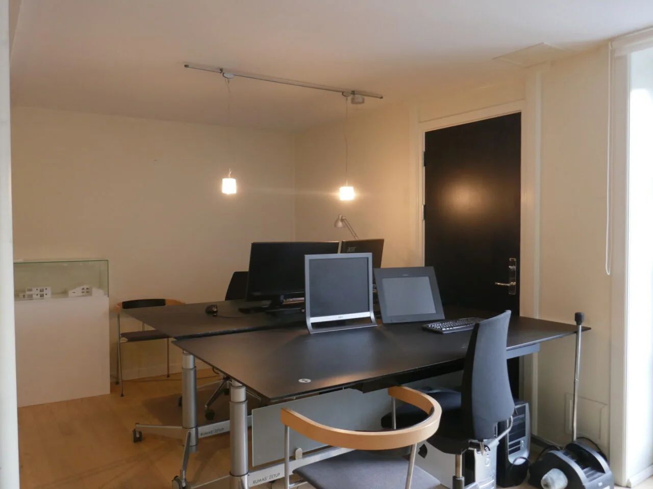 Kontor med to borde, hver med to skærme, en lampe, to skrivebordsstole og en computer med tangentbord