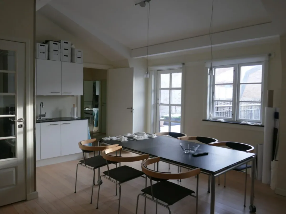 Moderne køkken med højloft, lysevinduer, højloftsvinduer og massivt trægulv. Vægge og møbler er hvide, og der er en