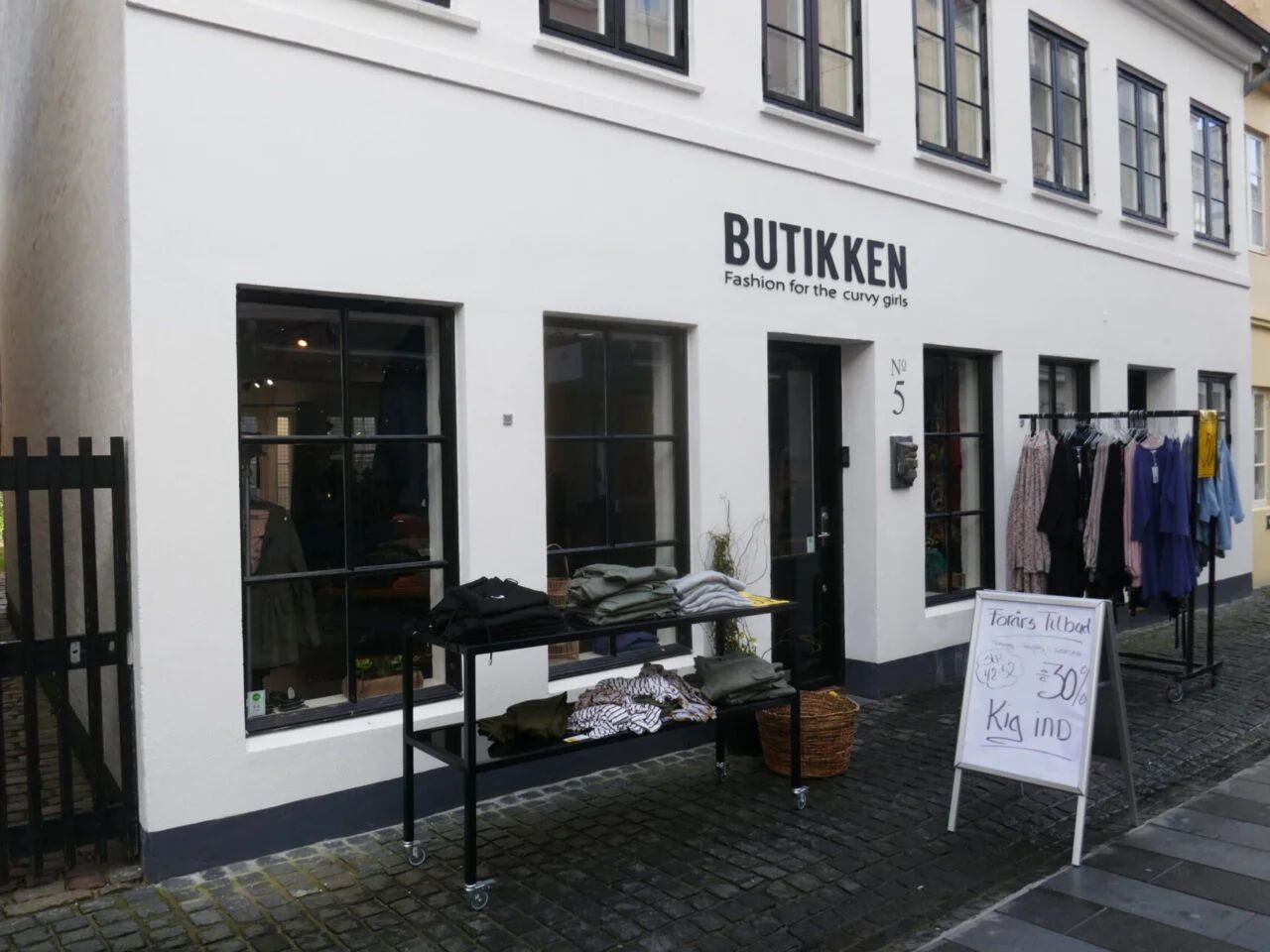 Butik Butikkken med mode til kurvede kvinder, og en sort vogn med tøj og en hængeklædeskab udenfor.